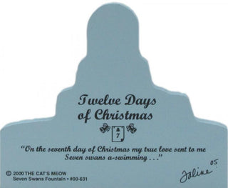A light blue back of wooden replica with  printed with the text 'Twelve Days of Christmas,' a quote, '© 2000 THE CAT'S MEOW,' 'Seven Swans Fountain,' and a signature on a white background.