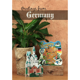 Two wooden replicas shaped like a castle and a map of Germany on a wooden surface with a plant in the background.