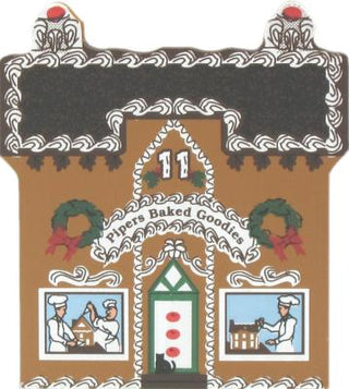 3/4" thick wooden replica of A gingerbread house featuring the text 'Fivers Baked Goodies' across the front, with decorative white icing-style borders, green wreaths, red bows, and small illustrated windows showing chefs working.