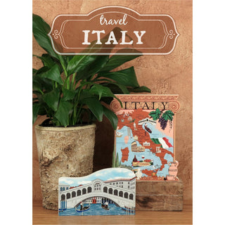 Decorative items with 'Travel Italy' theme on a wooden surface with a plant.
