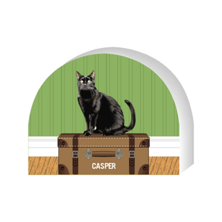 Wooden replica of a Black cat sitting on a suitcase with 'Casper' labeled, against a green wall in the  background.