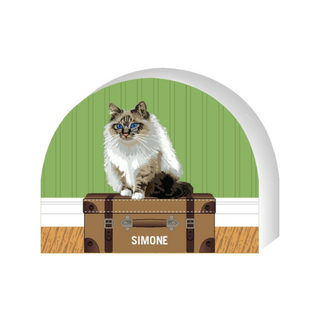 Wooden replica of a  Cat named Simone sitting on a suitcase with a green wall in the background
