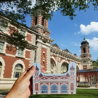 Hand holding a cutout of Ellis Island against the actual building