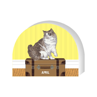 Wooden replica of a  Cat on a suitcase with 'April' text against a yellow background
