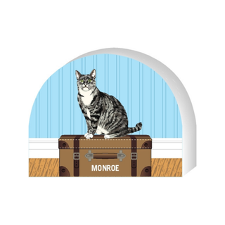 Wooden replica of a Cat sitting on a suitcase with 'Monroe' labeled, against a blue door background