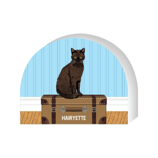 Wooden replica of a Illustration of a cat on a suitcase with 'HARLYETTE' on it, set against a blue wall.