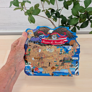 hand holding 3/4" thick wooden map of the USA with an eagle and banner saying America the Beautiful