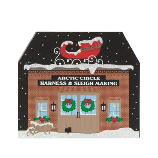 3/4" thick wooden replica with an illustration of a  building with 'Arctic Circle Harness & Sleigh Making' sign, decorated for Christmas.