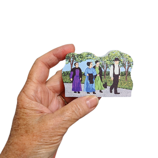 hand holding a 3/4" wooden replica of a group of amish walking on a road