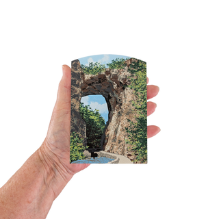 Hand holding a 3/4" thick wooden illustration of a natural bridge on a white background.