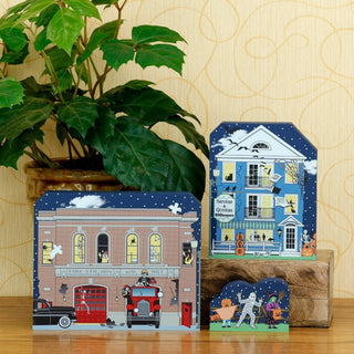3/4" thick wooden Decorative house-shaped cards with festive designs on a wooden surface with a plant in the background.