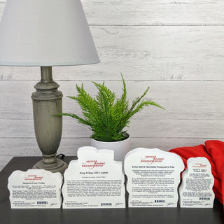 Four white product labels on a dark surface with a lamp and plant in the background.