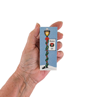 Hand holding a 3/4" thick wooden illustration of a lamppost with Christmas decor