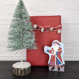 Red gift box with decorative string, small Christmas tree, and Santa Claus figure on a wooden surface.