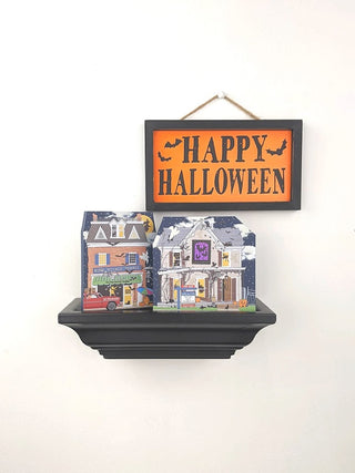 Decorative shelf with 'Happy Halloween' sign and small houses on a white background