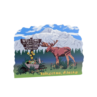 wooden replica with an illustration with a Wooden sign that says  with a deer and mountain landscape, featuring text on a blue sky background.welcome to beautiful downtown talkeetna'