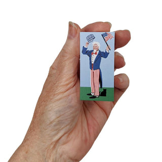 Hand holding a 3/4" Wooden replica with a illustration of a character in a suit and hat, waving an American flag.