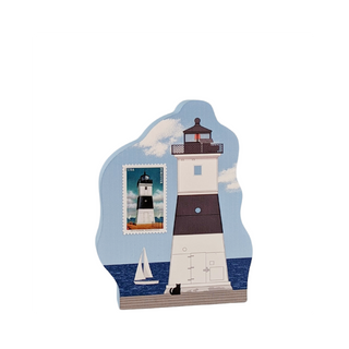 A decorative lighthouse-shaped wooden plaque featuring a stylized lighthouse illustration, a postage stamp design, a small sailboat, and a black cat on a blue sky and ocean background.