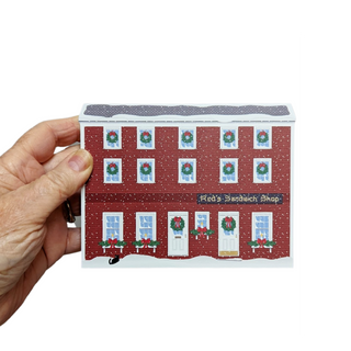 Hand holding a small 3/4" thick wooden building with Christmas-themed windows.