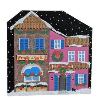 3/4" thick wooden replica with an illustration of a  Christmas scene with two colorful buildings, 'Wreaths & Garland' and 'Fine Crafters', against a snowy background.