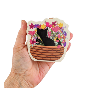 Hand holding a 3/4" thick wooden cutoutof a black cat in a basket with flowers.