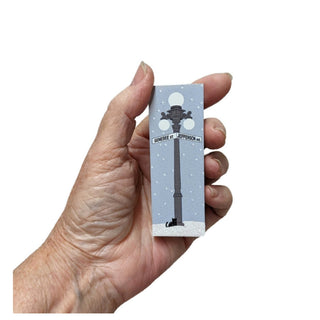 Hand holding a small rectangular card with a design of a street lamp and text on a white background