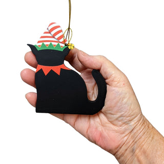 Hand holding a black cat-shaped ornament with festive hat and collar on a white background
