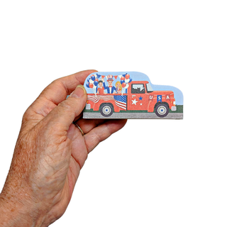 hand holding 3/4" thick wooden replica of a patriotic truck with american flags