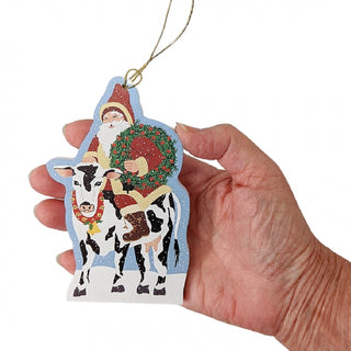 Hand holding a Christmas ornament with Santa Claus and a cow.