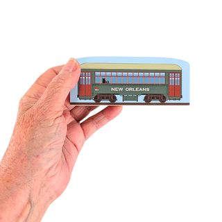 Hand holding a 3/4" thick wooden model of a New Orleans streetcar on a white background