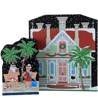 Two Christmas-themed wooden replicas: one with a house and palm trees, the other with two people on a bench.