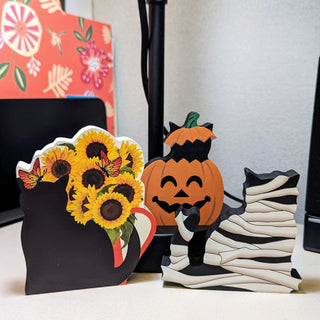 Decorative items including a black cat, sunflowers, a pumpkin, and a zebra-striped cat on a white surface.