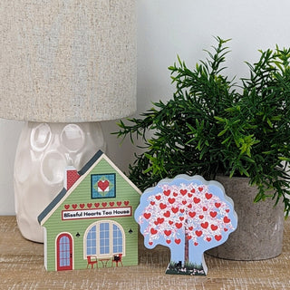 Decorative house and tree with heart designs on a surface with a lamp and plant in the background.