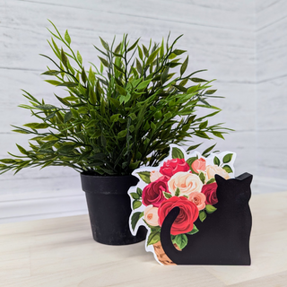 Black cat-shaped 3/4" thick wooden cutout  with floral design next to a potted plant on a light wooden surface.