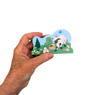 Hand holding a small wooden replica with a lamb and Easter eggs illustration on a white background
