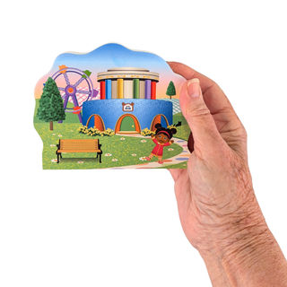 Hand holding 3/4" thick Wooden replica of Daniel Tiger's Neighborhood, Museum-Go-Round handcrafted by The Cat's Meow Village in the USA. Licensed by Fred Rogers Productions & PBS Kids.