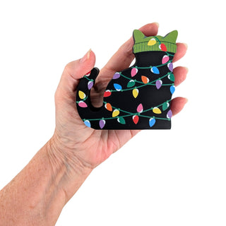 hand holding 3/4" thick wooden replica of a black cat with a green beanie on all tangled up in christmas lights