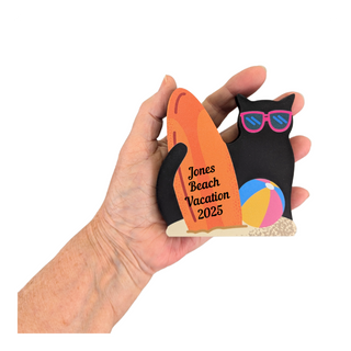Hand holding a decorative magnet with 'Jones Beach Vacation 2025' text, a cat design, and beach ball.