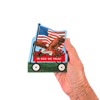 A hand holding a 3/4" thick wooden replica  featuring an American flag, an eagle, red roses, and the text 'IN GOD WE TRUST' on a white background.