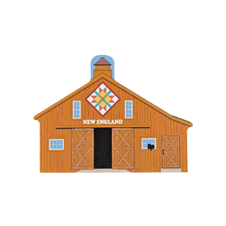 3/4" thick wooden replica with an illustration of a wooden barn with the words "NEW ENGLAND" above the central door. The barn is rendered in warm brown and orange wood tones, with a multicolor quilt-pattern motif on the gable, small windows, and a black doorway.