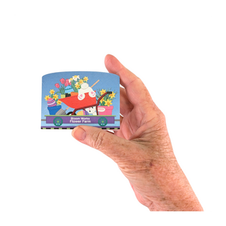 Hand holding a small wooden replica with a colorful illustration of a flower truck and flowers on a white background