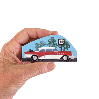 Hand holding 3/4" thick wooden model of a classic car with Route 66 sign in the background. 