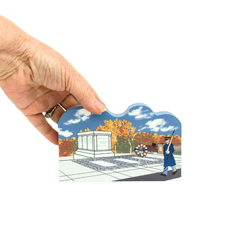 Hand holding a 3/4" thick wooden model of a memorial with trees and a person in uniform.