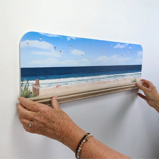 Person holding a beach scene print against a white wall