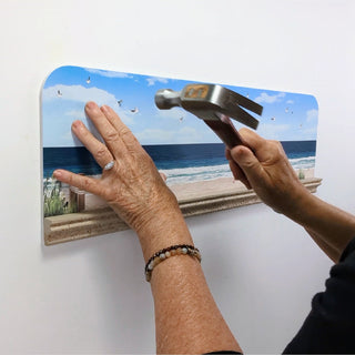 Person using a hammer to remove a decorative wall piece with a beach scene.