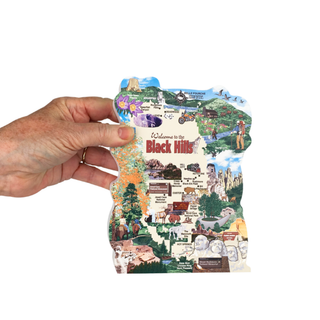 Hand holding a colorful 3/4" thick wooden cutout map of the Black Hills region with various attractions and landscapes.