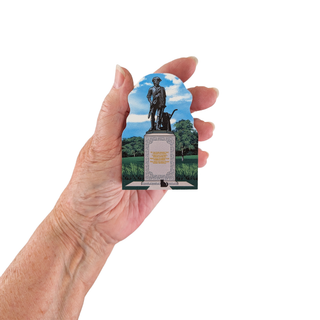 Hand holding a 3/4" wooden replica with an illustration of a statue and plaque with trees and sky in the background