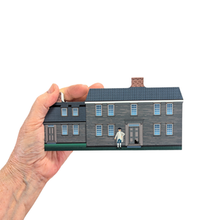 Hand holding a 3/4" wooden replica with an illustration of a house with a person and dog in front.