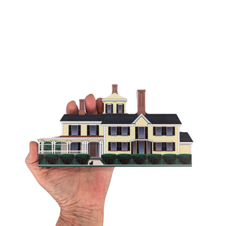Hand holding a miniature model of a large house with a white background