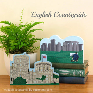 Wooden keepsakes depicting Stonehenge and Windsor Castle on a wooden surface with a plant in the background.